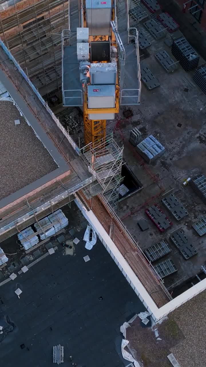 Portrait top-down drone shot of yellow crane over derelict urban construction site