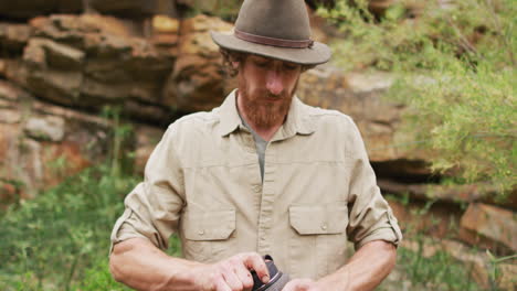 portrait of bearded caucasian male survivalist screwing cap on water bottle in wilderness