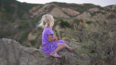 Little-Girl-Sits-on-Rock-and-Looks-at-Mountains