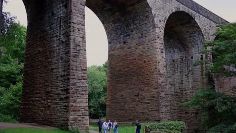 large arched bridge shot frpm low down with moving trees and walkers passing by