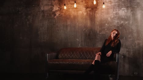 woman in a black dress sitting on a leather couch in a dark studio