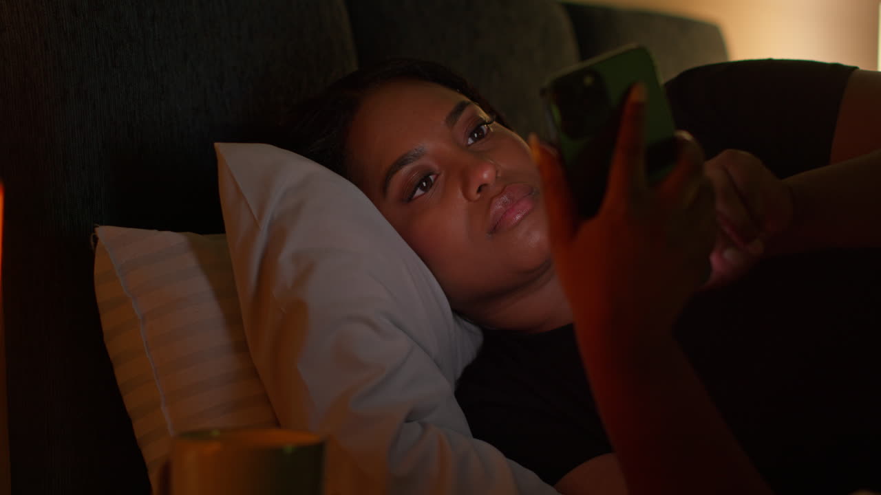 Woman using phone in bed at night