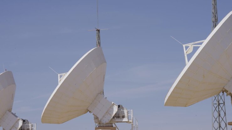 A row of modern telecommunications antennas at a ground station is aimed upwards, ready to send and receive data from orbiting satellites