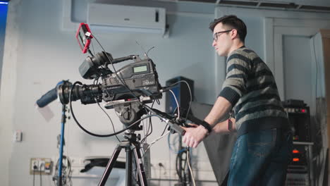 man adjusting professional video camera on tripod in studio. technician focused on camera setup with screen and equipment. filming session ongoing in production environment