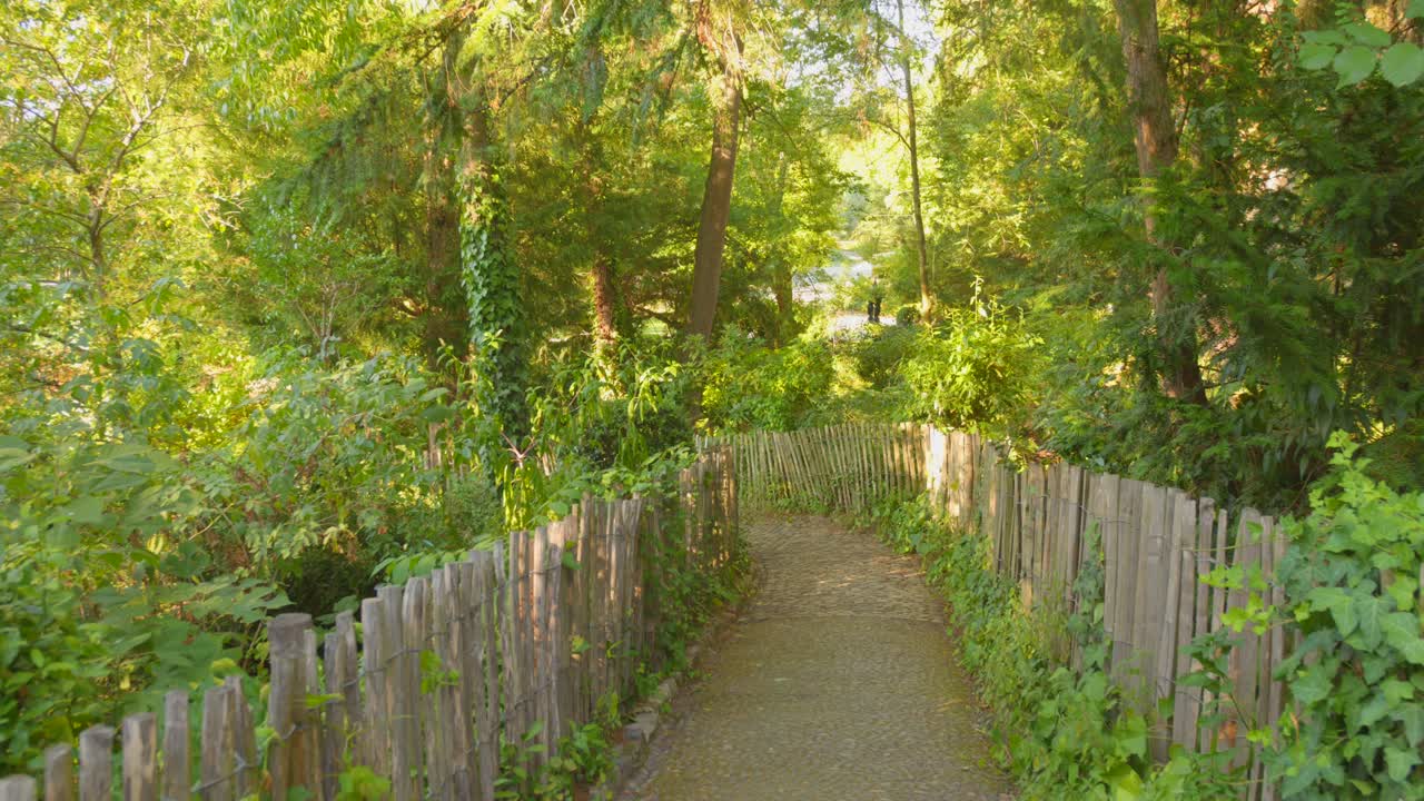Profile view dirt path framed with wooden fence with lush, green foliage during daytime of Botanical garden in Toulouse, France