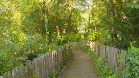 profile view dirt path framed with wooden fence with lush, green foliage during daytime of botanical garden in toulouse, france