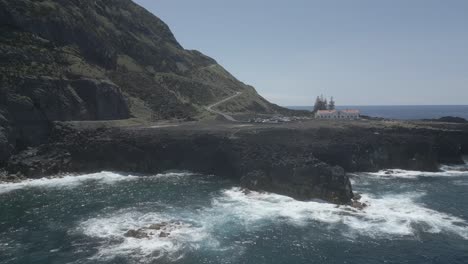 Lighthouse-on-rocky-coast-with-waves-crashing-on-a-sunny-day