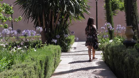 girl walking through a peaceful park, stops to smell a flower, then shares a warm glance with the camera