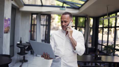 Und-Ein-Erwachsener-Mann-Im-Hemd-Geht-Mit-Einem-Laptop-Durch-Ein-Restaurant-Und-Telefoniert