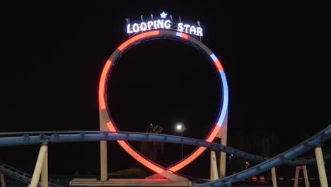 tiro nocturno estático del parque de atracciones de un circuito de montaña rusa con luces intermitentes que pasan rápido por la cámara