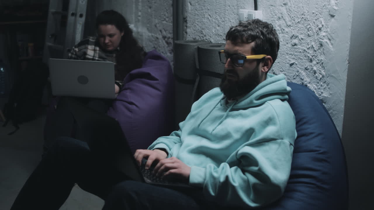 Two people working on laptops in a basement home office.