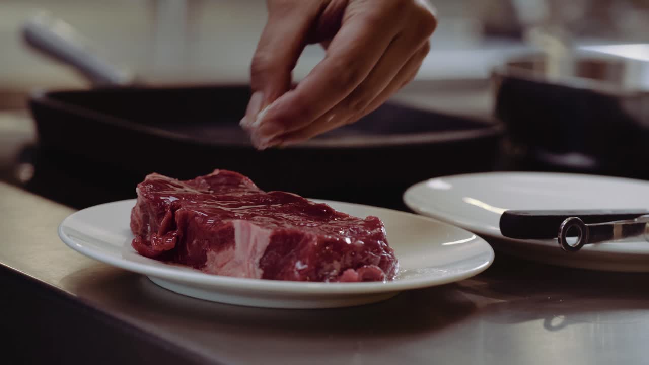 CLOSE UP: Seasoning Steak with salt. Pouring salt on a steak fillet on a plate