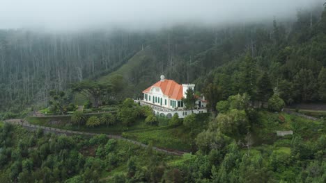 beautiful villa on slope of lush mountains below clouds in madeira, aerial