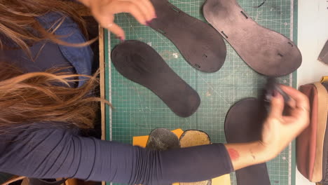 vertical time lapse female shoemaker brushing stain onto sole shaped pieces in workshop