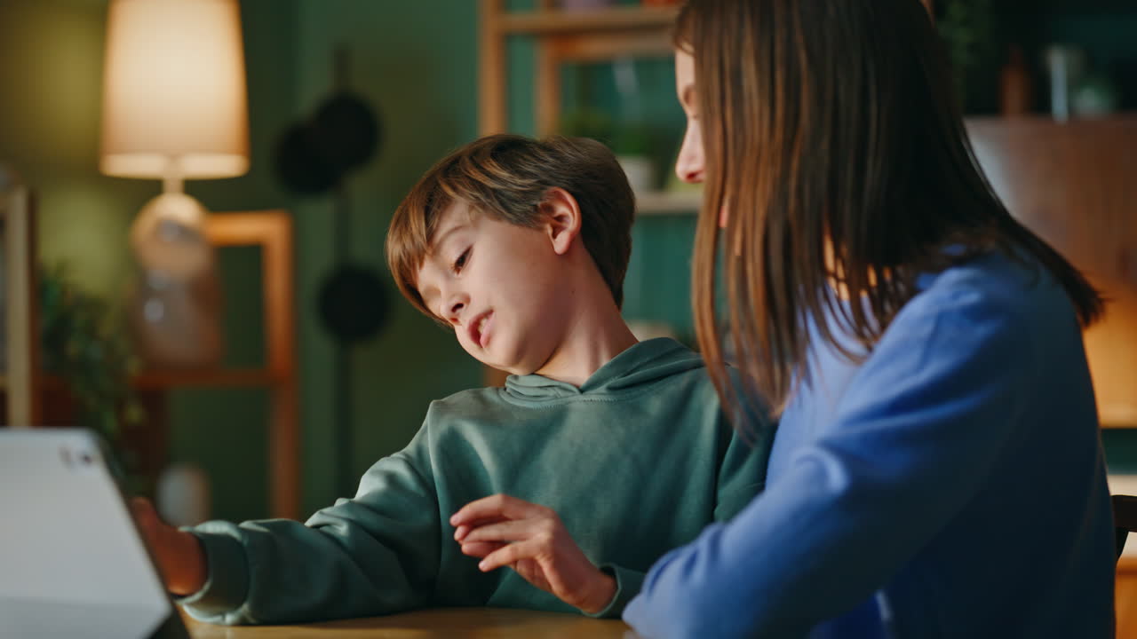Primo piano di madre e figlio che giocano al tablet seduti insieme alla scrivania di casa. Mamma e figlio sorridenti