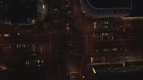 AERIAL:-Beautiful-Overhead-Shot-of-busy-intersection-at-night-with-Car-traffic-and-city-lights