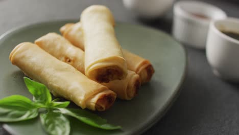 composition of plate with spring rolls and chilli sauce on grey background