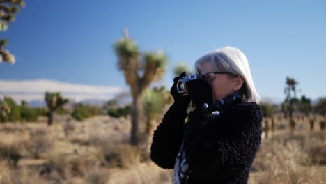 An-older-adult-woman-photographer-taking-pictures-with-her-old-fashioned-film-camera-in-a-desert-wildlife-landscape