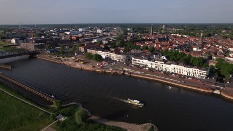 seguimiento aéreo de transporte interior gran buque de carga dejando ondas en el río ijssel pasando ijsselkade boulevard semblante paisaje urbano de la ciudad de la torre zutphen