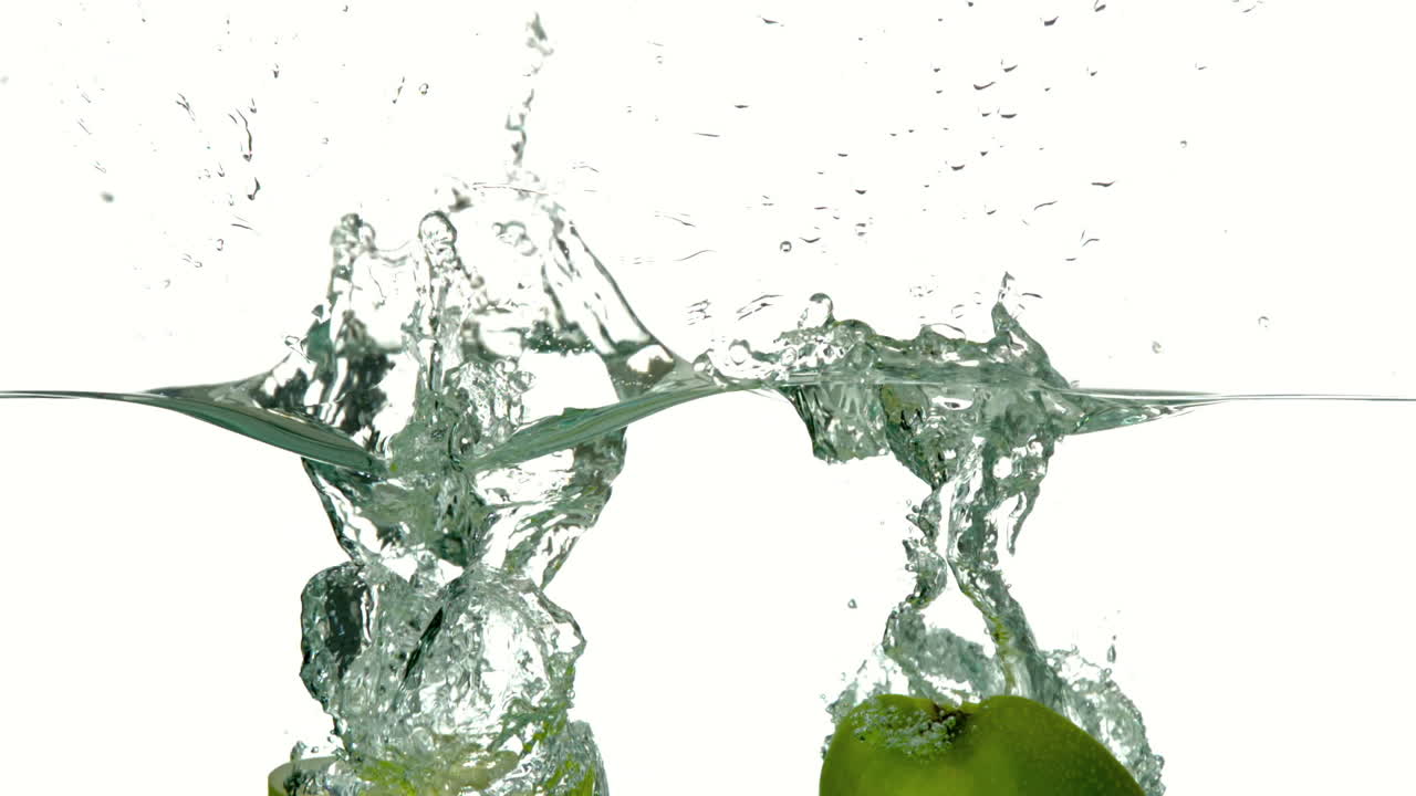 Apple halves plunging into water on white background