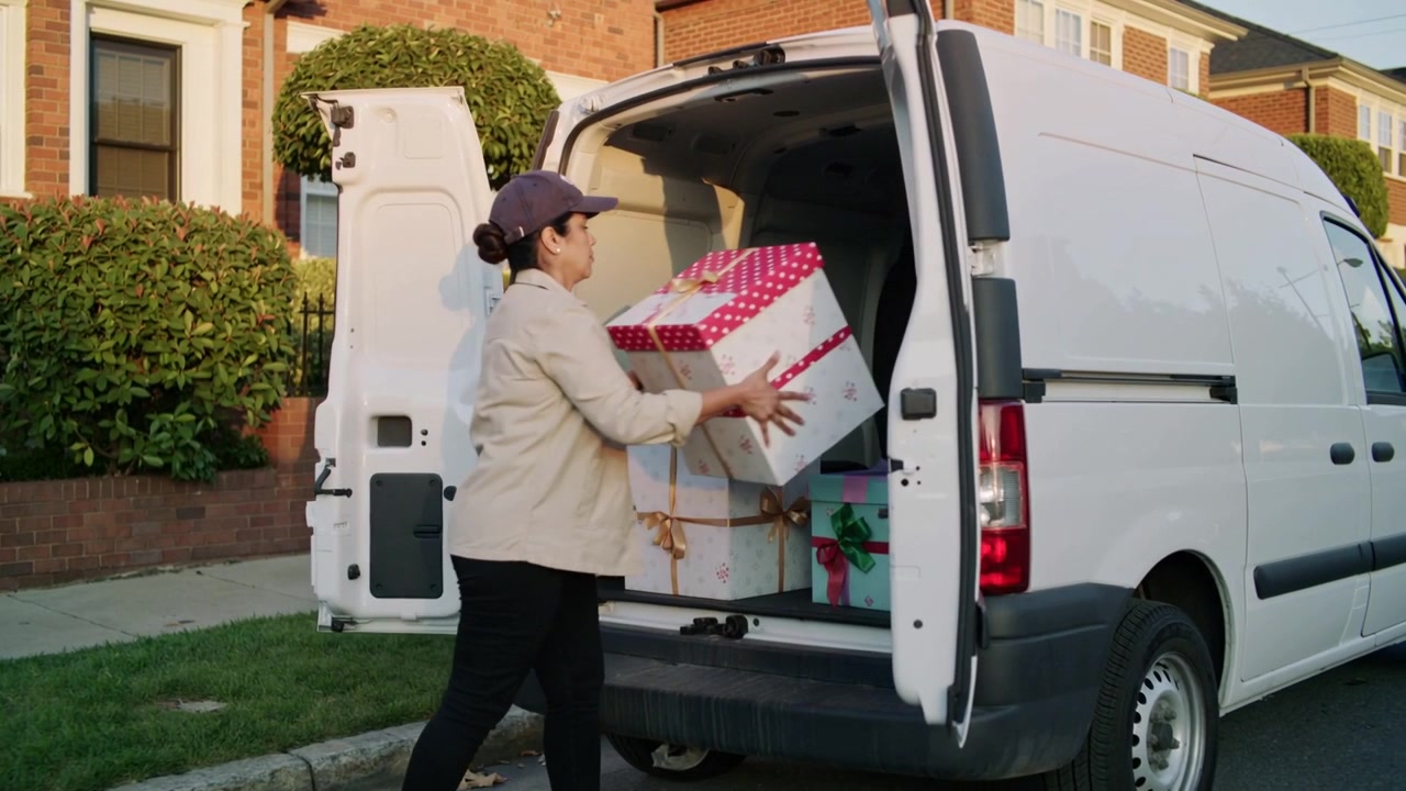 Reaching into open white van at curb courier lifting, sliding polka-dot box delivering, wearing cap