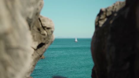 peaceful ocean shore view with sailboat passing by through rock cliff under blue sky at cascais portugal 4k steady shot