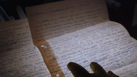 hands of a forensic specialist wearing protective gloves examine handwritten letters on a backlit table