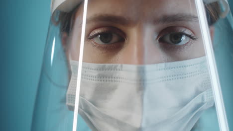 médico femenino con escudo facial y máscara posando para la cámara