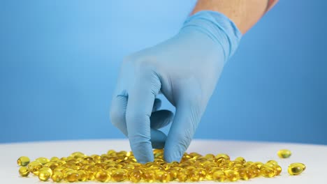 pile of omega fish oil capsules, caucasian hand with blue gloves picks one up