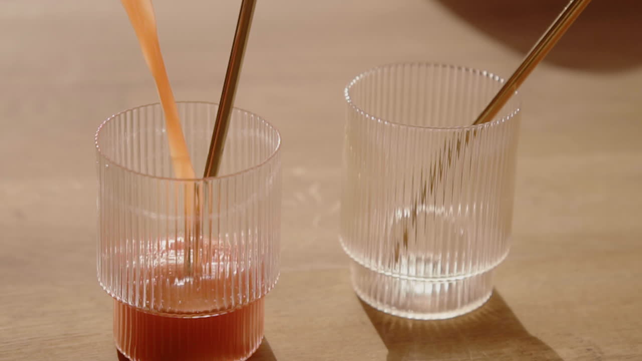 A Orange Cold Pressed Juice getting poured into a drinking glass with a metal straw in Slow Motion during Detox Cleanse