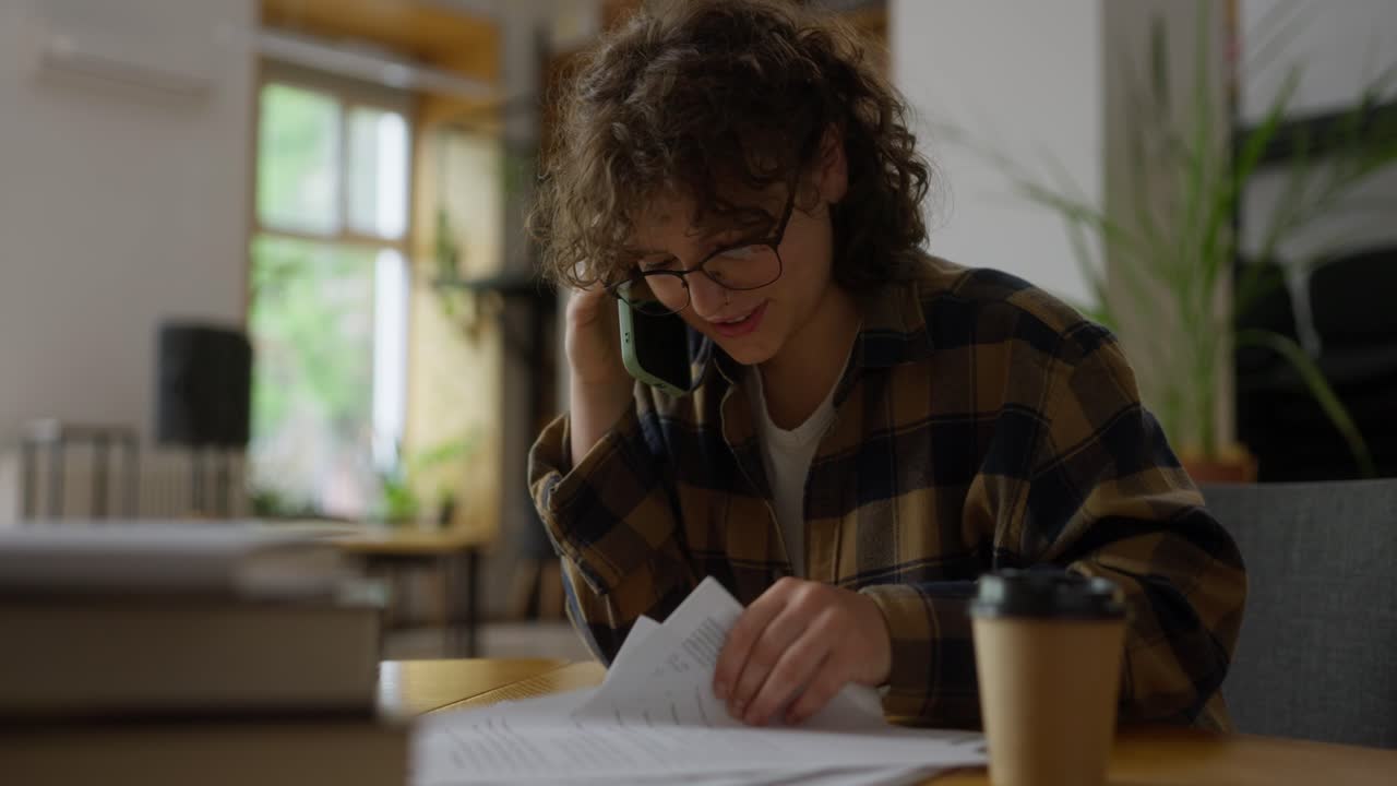 Happy girl student communicates on the phone and reads documentation while sitting at a table in the library