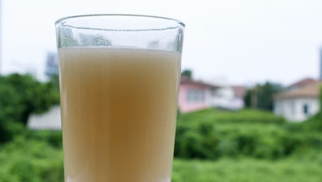 Sprudelndes-Wasser-In-Einem-Glas,-Das-Durch-Die-Verdünnung-Eines-Antazidums-Oder-Natriumbikarbonats-Entsteht,-Vor-Dem-Hintergrund-Von-Häusern-Und-Grüner-Vegetation,-Die-Unscharf-Sind