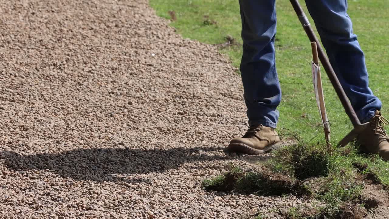 persona redefiniendo el borde de hierba de un camino de grava.
