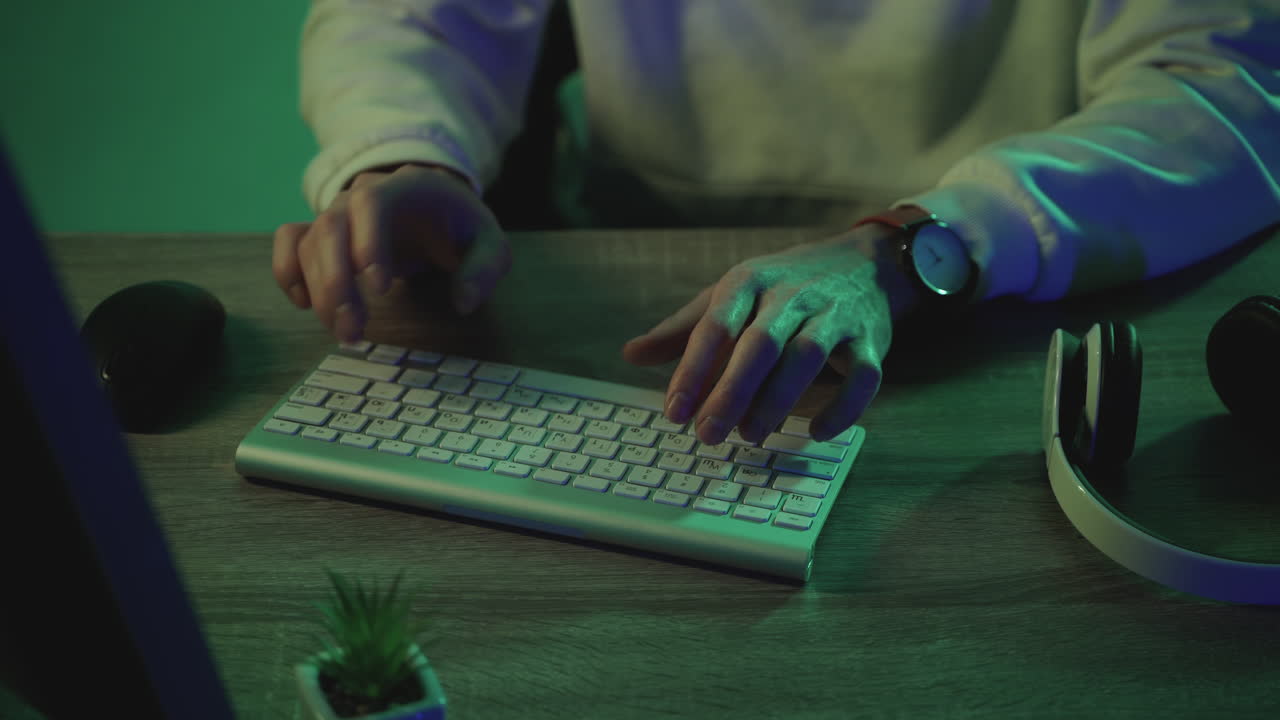 мужские руки печатают на клавиатуре, работая с компьютером на красочном фоне.