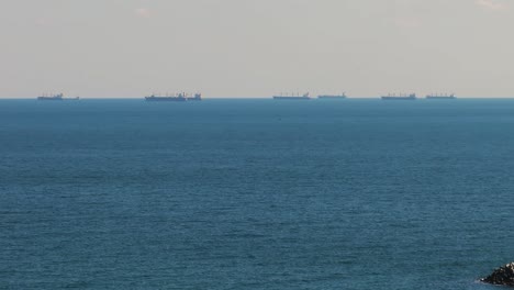 Drone-zoomed-shot,-over-the-blue-sea-reveals-the-boundless-horizon-showing-stationary-big-ships-4K60Fps