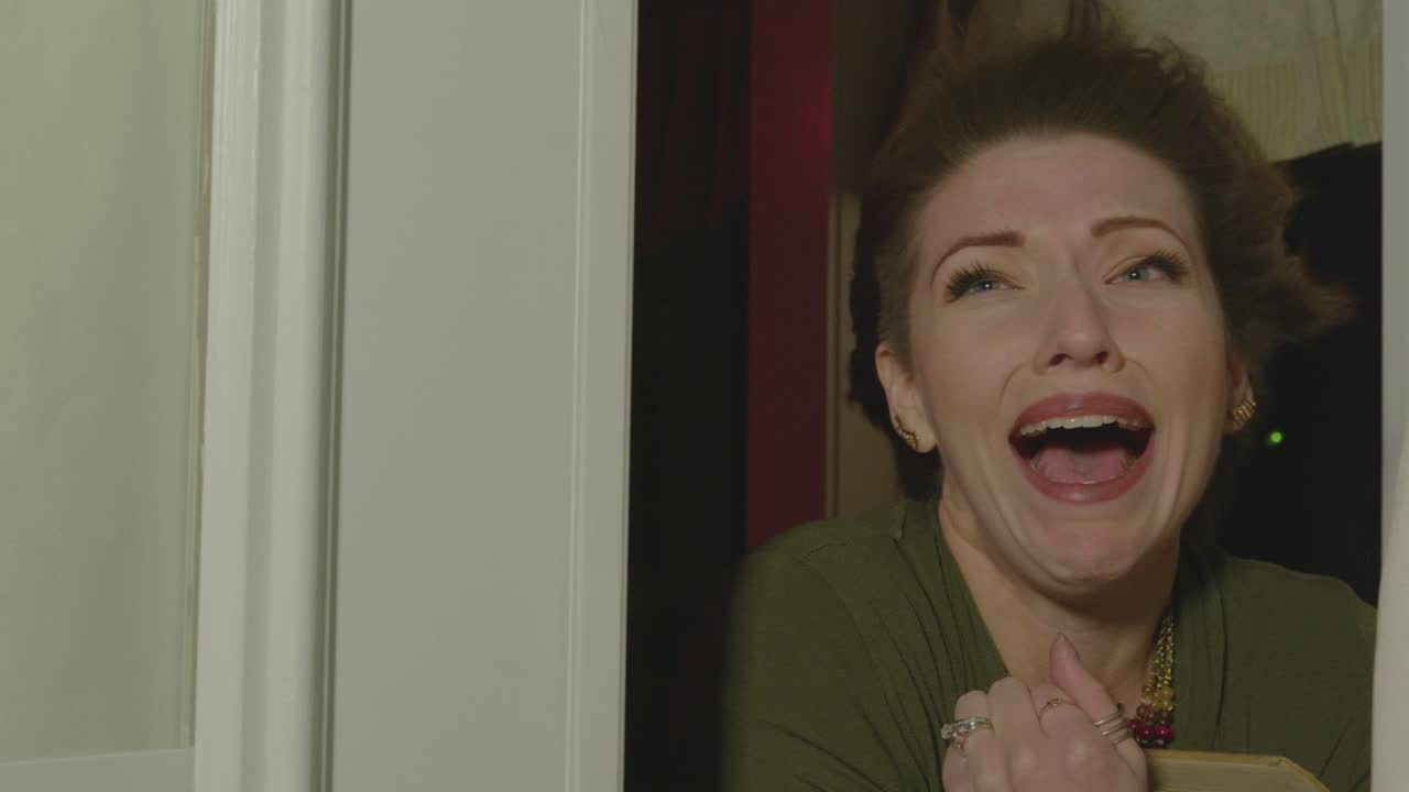 A woman is seen screaming in a doorway. Her hair is blowing back and the door slams in her face. in a haunted house. She's really scared