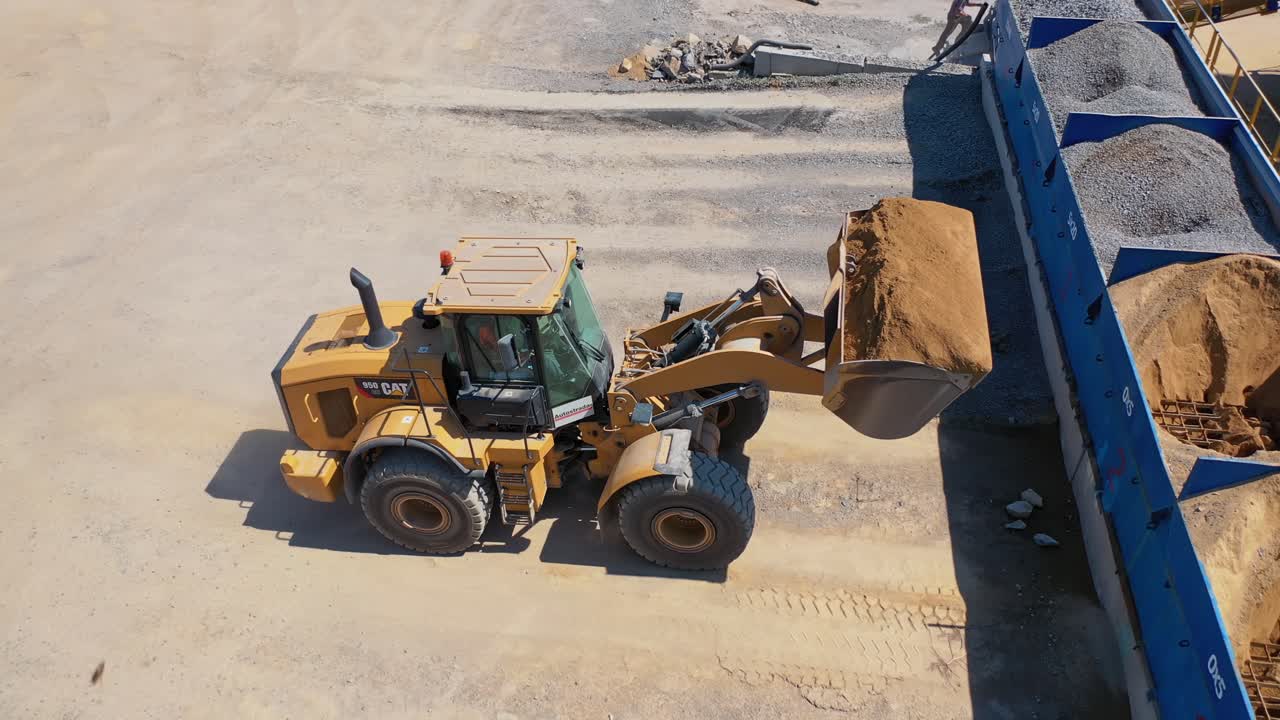Excavator on the territory of asphalt manufacture outdoors. Modern excavator pouring out sand from bucket into a special tank. Top view.