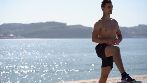 focused bare-chested man in shorts training at riverside