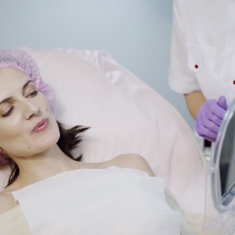a beautician takes a mirror in her hands and shows the result of the procedure for lip augmentation for the client at the cosmetology center. a woman looks on her lips after injections of botox in the reflection.