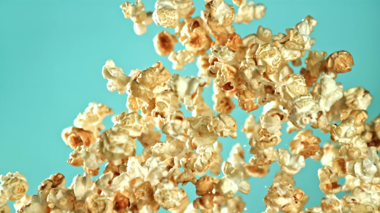 Golden Popcorn Flying Up in Slow Motion Against a Turquoise Background