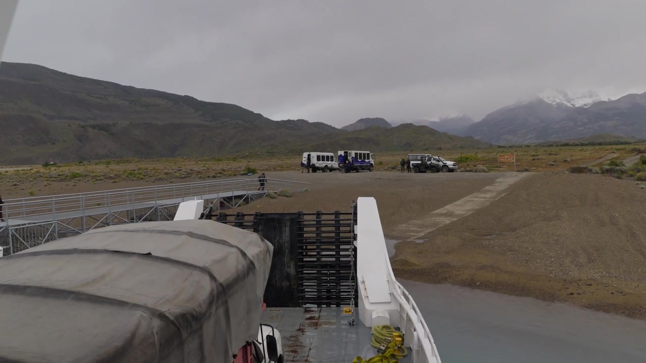 Embarcación de pasajeros llegando a un sitio de desembarco en el Lago Argentino, Santa Cruz, Argentina, con operaciones de transferencia en tierra, vehículos de expedición y paisajes glaciares dentro del Parque Nacional Los Glaciares.