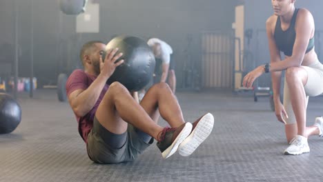entrenadora diversa motivando a un hombre determinado ejercitándose con una pelota de medicina en el gimnasio, en cámara lenta