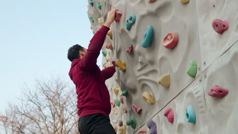 un hombre barbudo de treinta años sube a una pared de escalada en un campo deportivo al aire libre para fortalecer el agarre de la mano