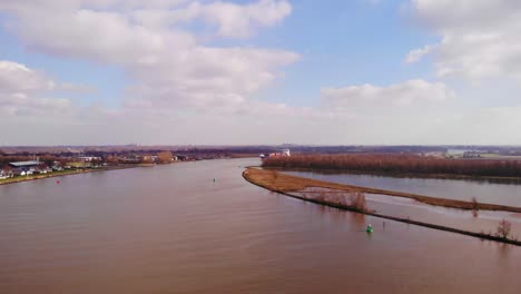 Aerial-Flying-Over-Oude-Maas-In-Barendrecht-With-Blue-Sky-And-Clouds-In-View-And-Cargo-Ship-Approaching-In-Distance