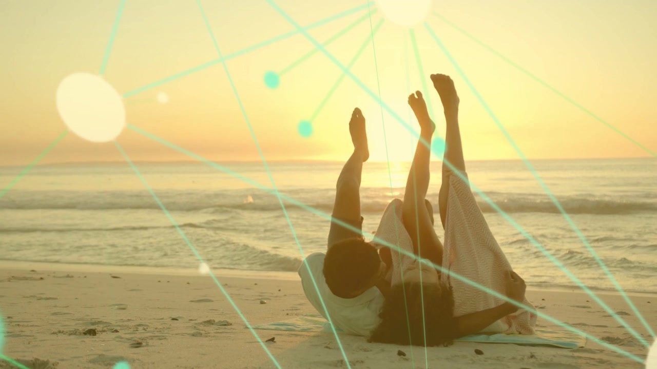 Man placing arm around woman, reclining and lifting legs on sunset beach with travel bokeh nodes