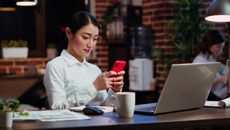 Smiling-employee-at-work-texting-friends-on-cellphone,-taking-break-from-tasks