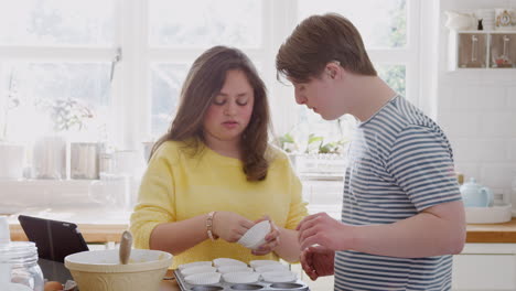 Una-Pareja-Joven-Con-Síndrome-De-Down-Poniendo-Cajas-De-Papel-Para-Cupcakes-En-Una-Bandeja-En-La-Cocina-De-Casa