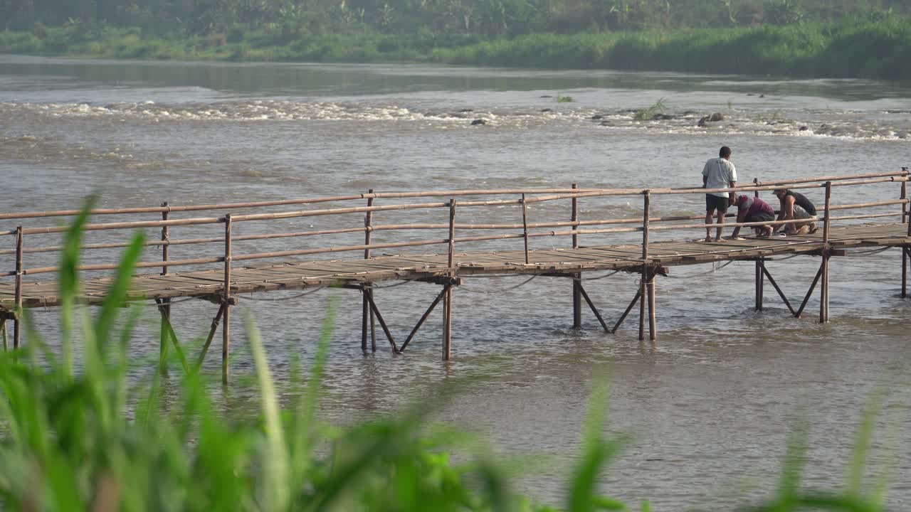 A group of people are maintaining and repairing a bridge made of wood. The bridge connects the villages of Bantul and Kulonprogo.