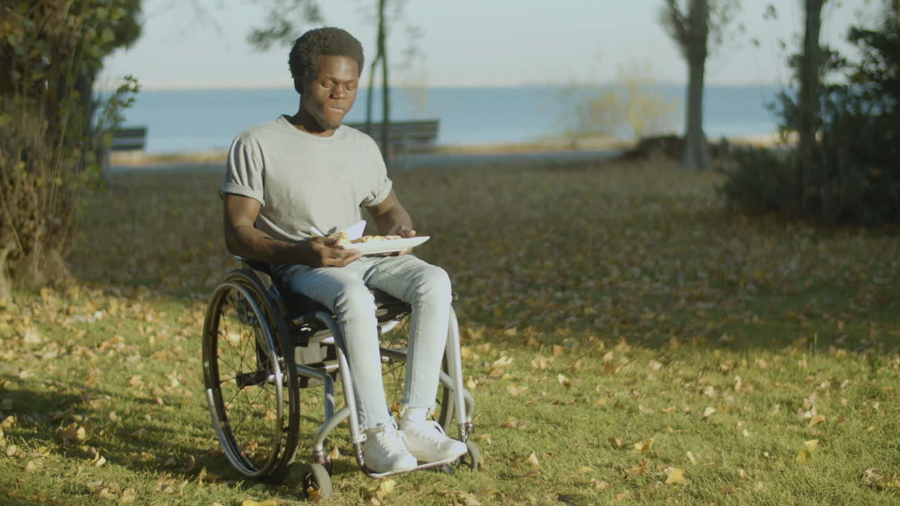 Young Black Man In Wheelchair Having Lunch In City Park 1