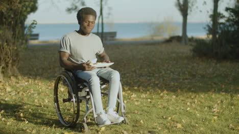 joven negro en silla de ruedas almorzando en el parque de la ciudad 1